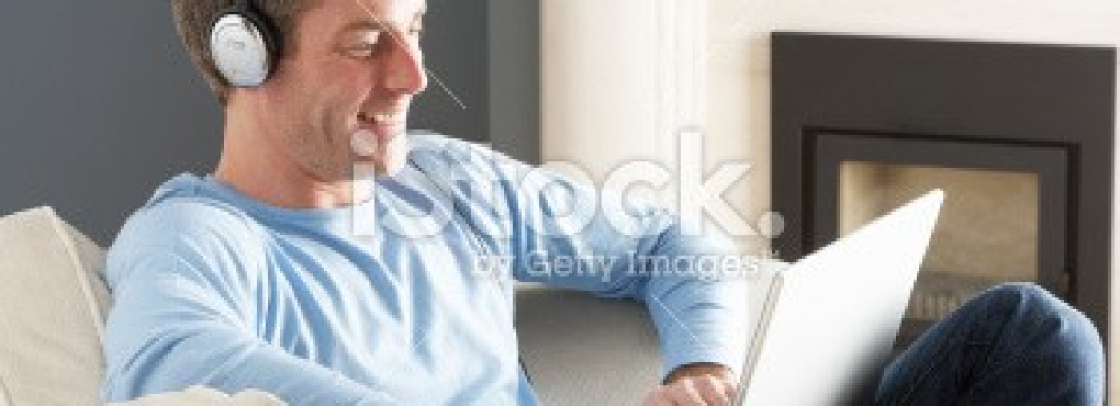 stock-photo-16026432-man-using-laptop-wearing-headphones-relaxing-sitting-on-sofa